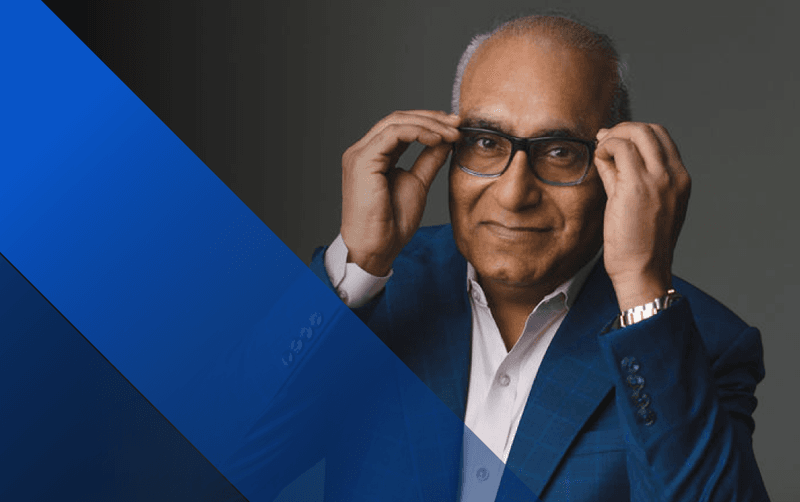 Elderly man with glasses adjusting them, wearing a suit.